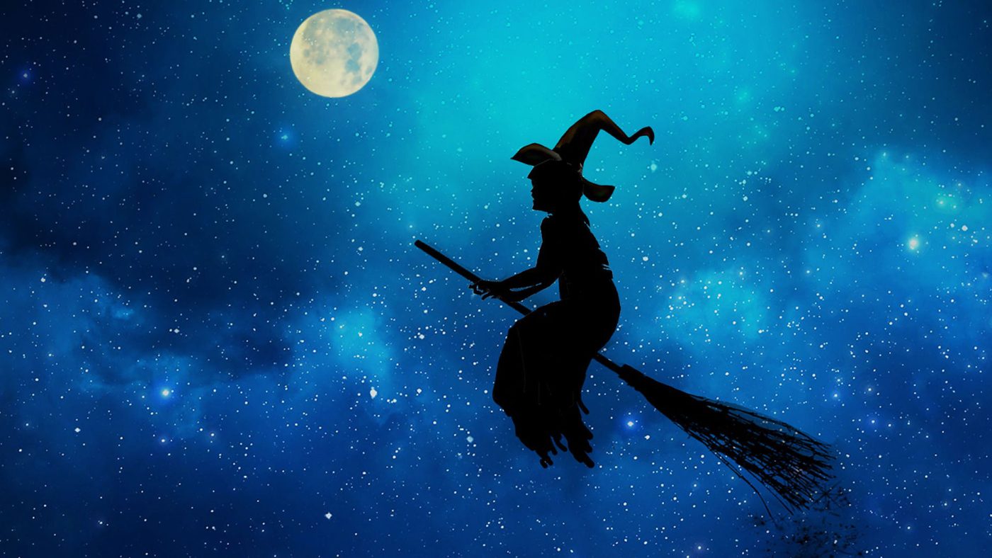 Silhouette della Befana che vola su una scopa sotto una luna piena e un cielo stellato.