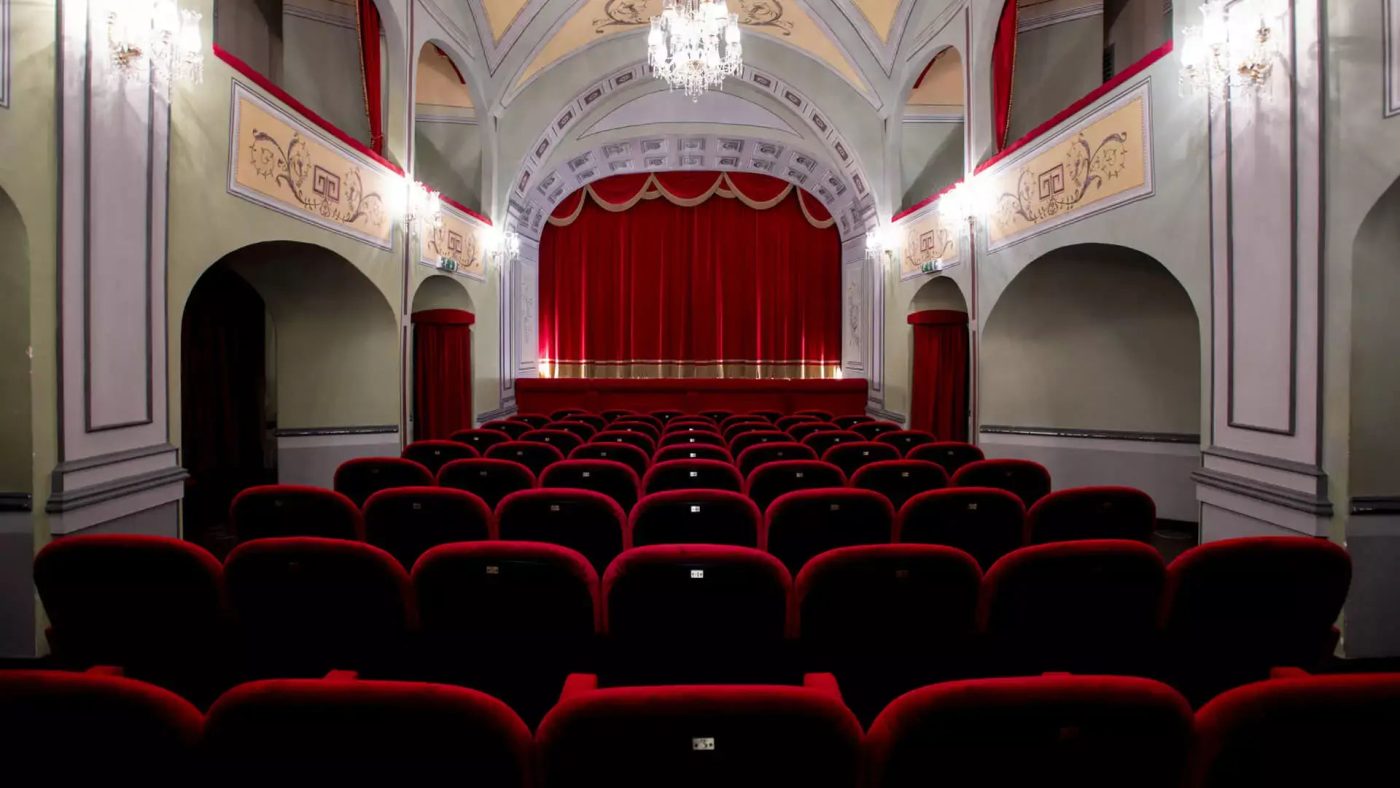 Interno del Teatro Donnafugata a Ragusa Ibla, con eleganti poltroncine rosse e un palco con sipario.