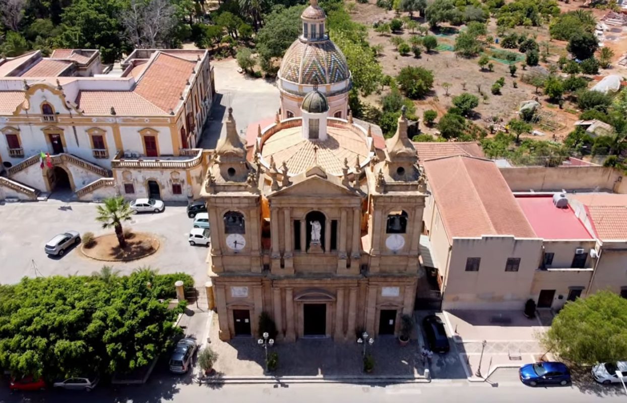 Veduta aerea della Chiesa Madre di Bagheria con la cupola maiolicata e le ville storiche circostanti immerse nel verde.